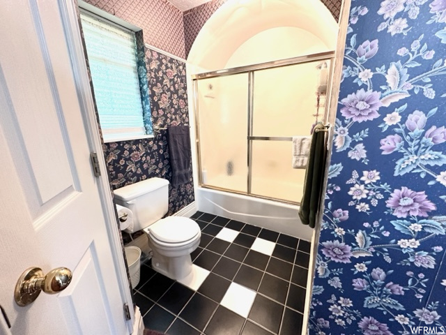Bathroom featuring tile floors, enclosed tub / shower combo, and toilet