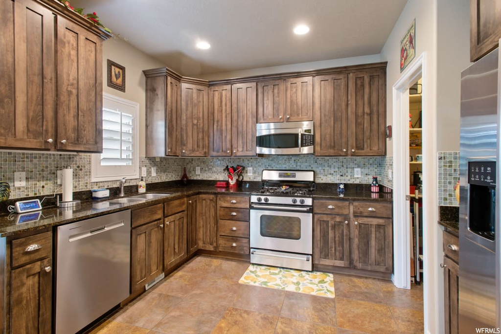 Kitchen featuring natural light, range oven, stainless steel appliances, light tile flooring, and dark stone countertops