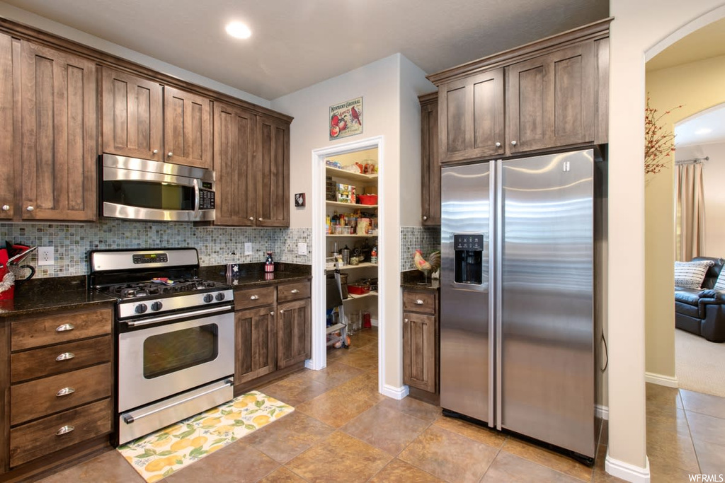 Kitchen featuring gas range oven, refrigerator, microwave, light flooring, and dark stone countertops