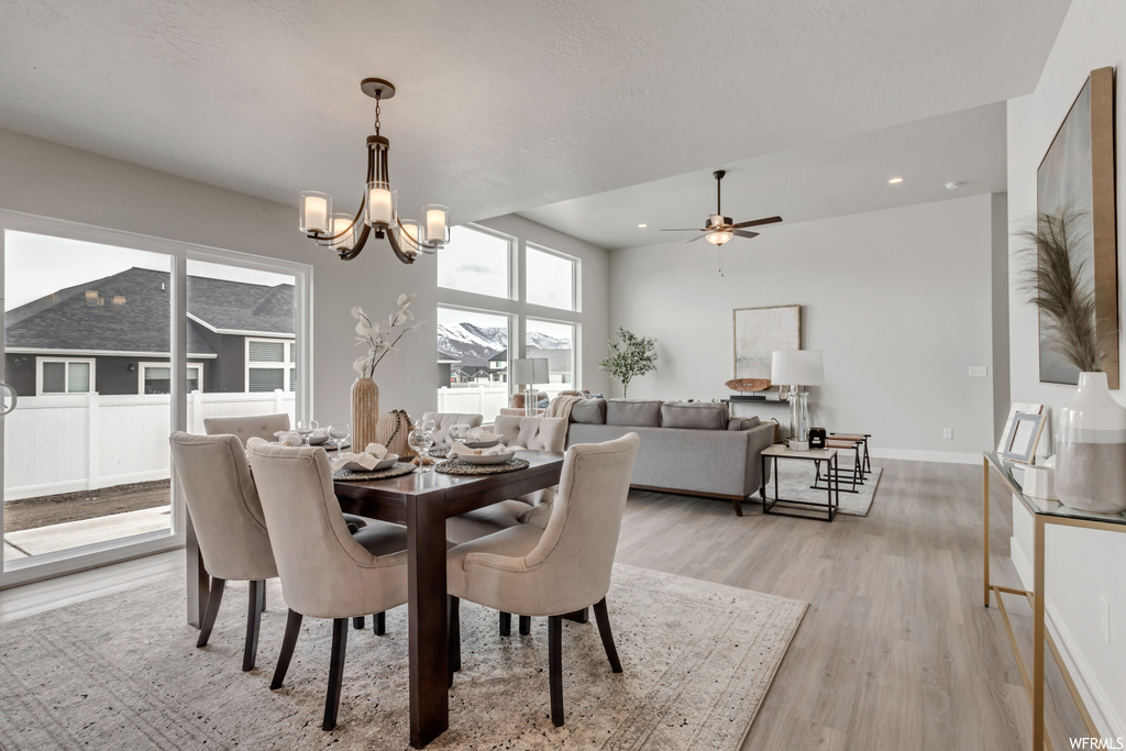 Dining area with natural light, hardwood flooring, and a ceiling fan with notable chandelier