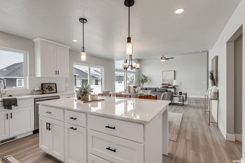 Kitchen featuring a healthy amount of sunlight, a center island, a ceiling fan, dishwasher, light parquet floors, pendant lighting, light countertops, and white cabinetry