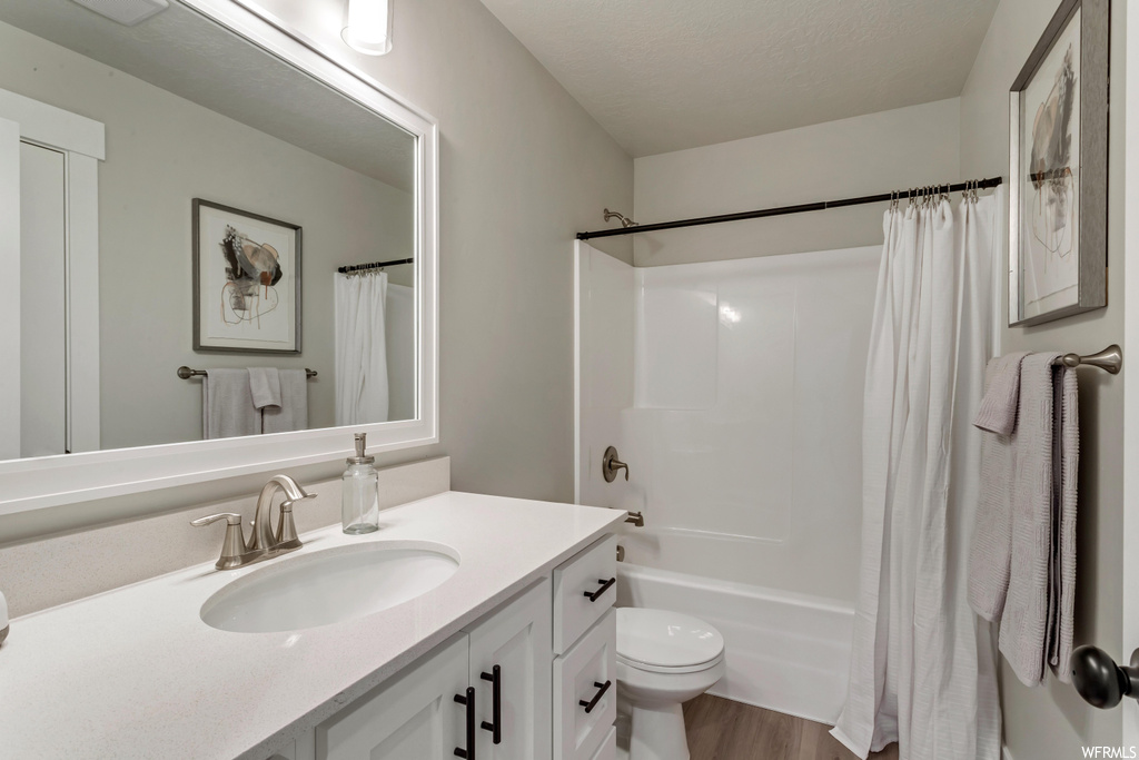 Full bathroom featuring hardwood flooring, vanity, shower curtain, mirror, toilet, and shower / bath combination