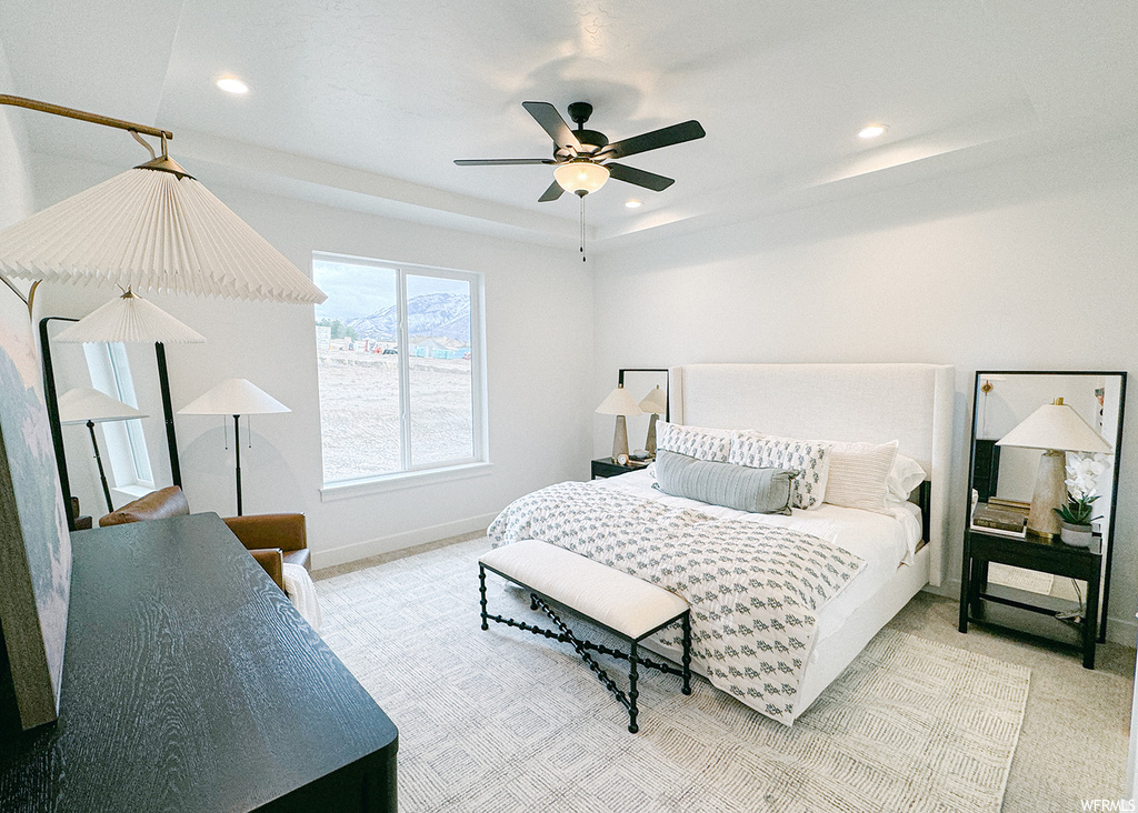 Bedroom with light colored carpet, ceiling fan, and a raised ceiling