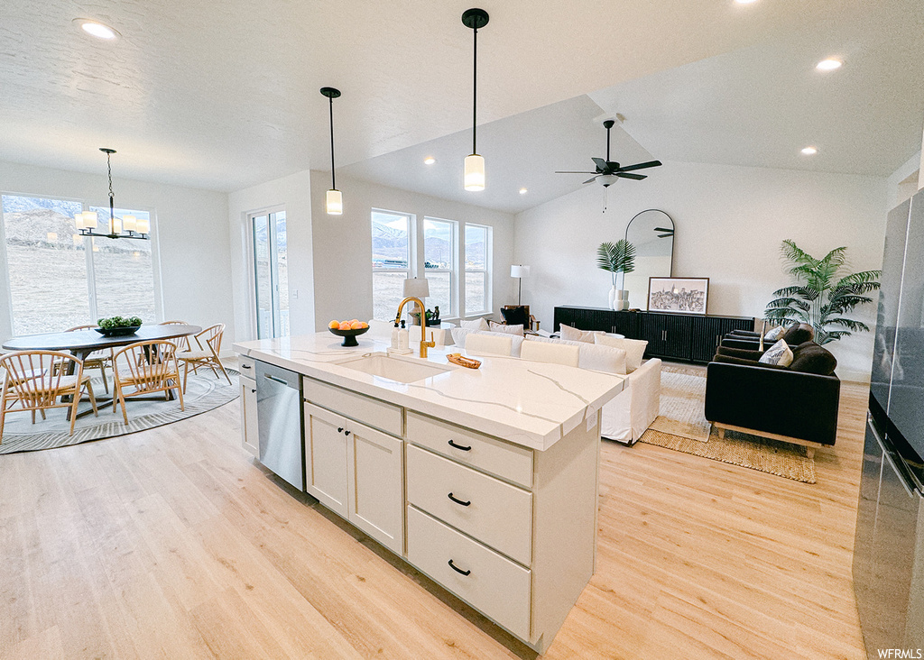 Kitchen featuring sink, light hardwood / wood-style flooring, ceiling fan with notable chandelier, dishwasher, and an island with sink