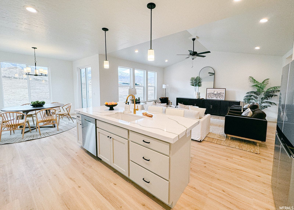 Kitchen with sink, light hardwood / wood-style flooring, ceiling fan with notable chandelier, a center island with sink, and stainless steel dishwasher