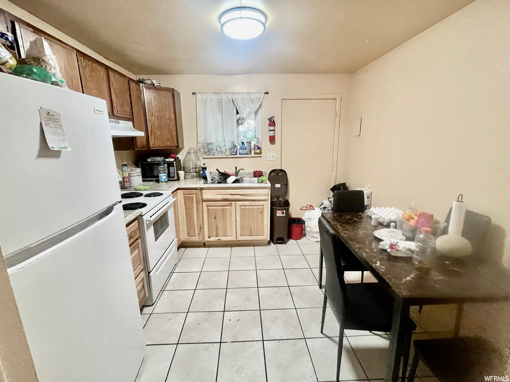 Kitchen featuring ventilation hood, electric range oven, refrigerator, and light tile flooring