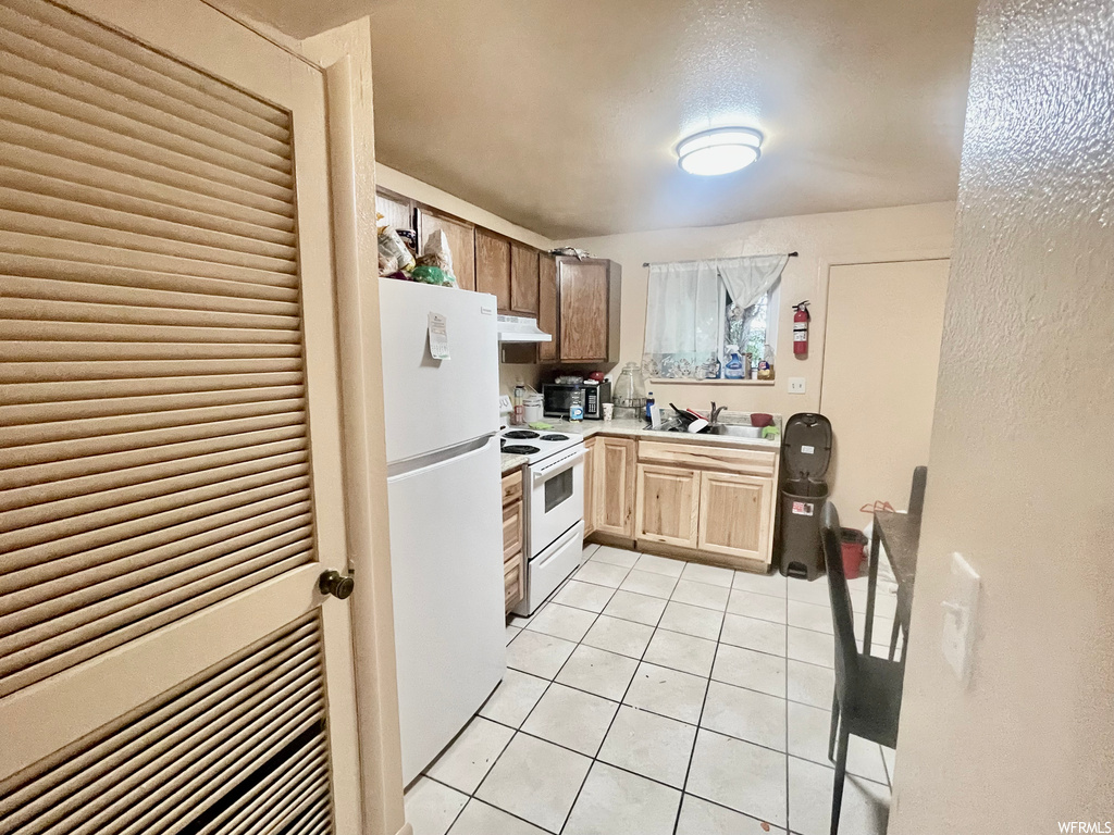 Kitchen with electric range oven, refrigerator, extractor fan, and light tile floors