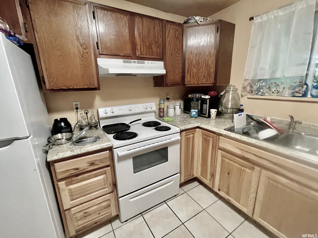 Kitchen with refrigerator, electric range oven, exhaust hood, light countertops, and light tile floors