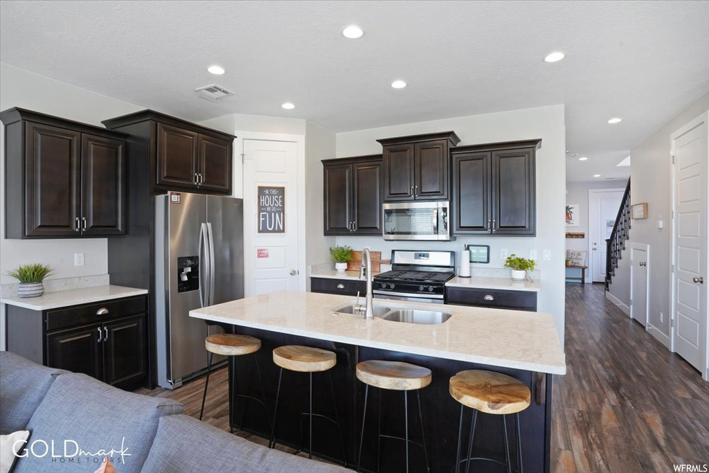 Kitchen featuring hardwood floors, a kitchen bar, gas range oven, stainless steel appliances, light countertops, a kitchen island with sink, and dark brown cabinets