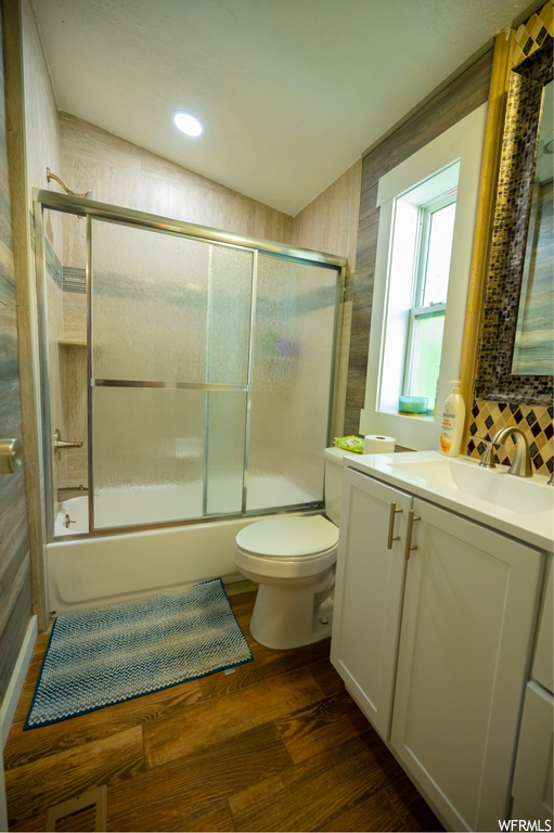 Full bathroom with natural light, hardwood floors, toilet, mirror, combined bath / shower with glass door, and vanity