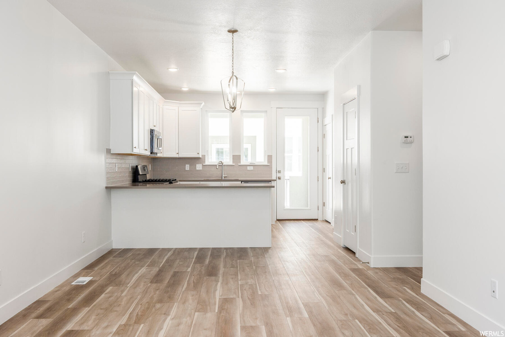 Kitchen with white cabinetry, range, backsplash, and light hardwood flooring