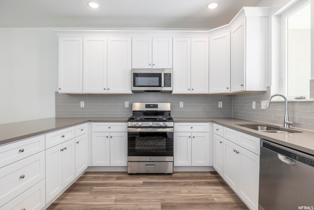 Kitchen featuring white cabinetry, backsplash, light countertops, light hardwood floors, and appliances with stainless steel finishes