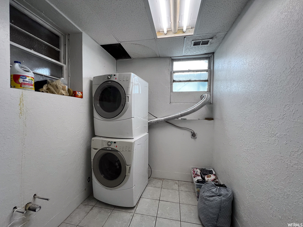 Laundry area with stacked washer / drying machine and light tile floors