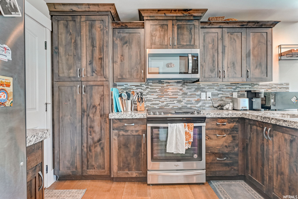 Kitchen with backsplash, light hardwood floors, light stone countertops, and stainless steel appliances