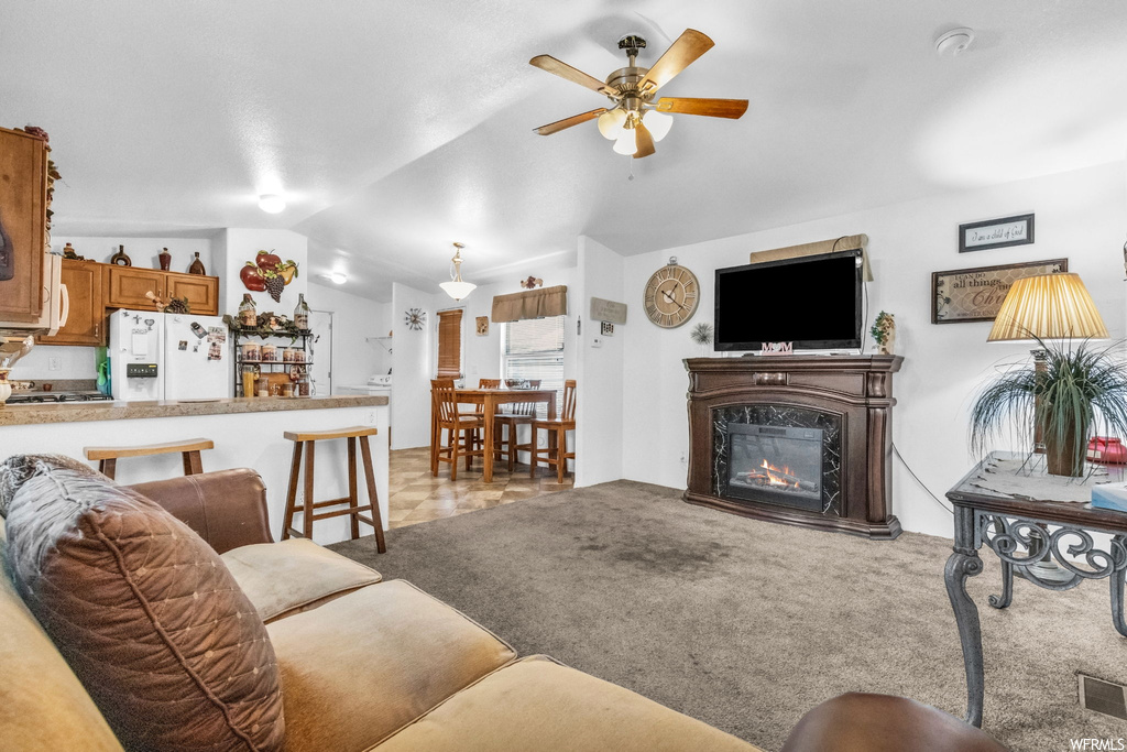 Living room featuring TV, ceiling fan, a fireplace, vaulted ceiling, and light carpet