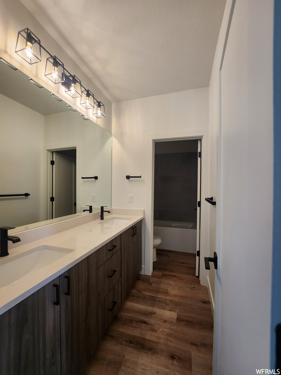 Bathroom featuring mirror, dark hardwood floors, double large sink vanity, and a bathing tub