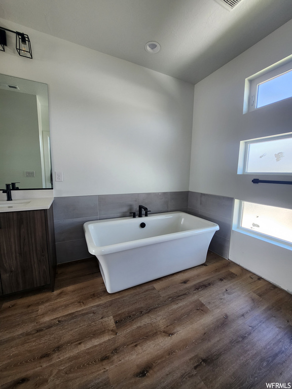 Bathroom featuring plenty of natural light, tile walls, a bath to relax in, vanity, dark hardwood floors, and mirror