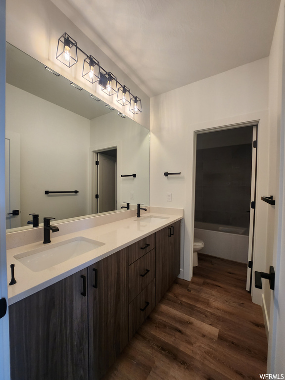 Bathroom with dual vanity, mirror, and dark hardwood flooring