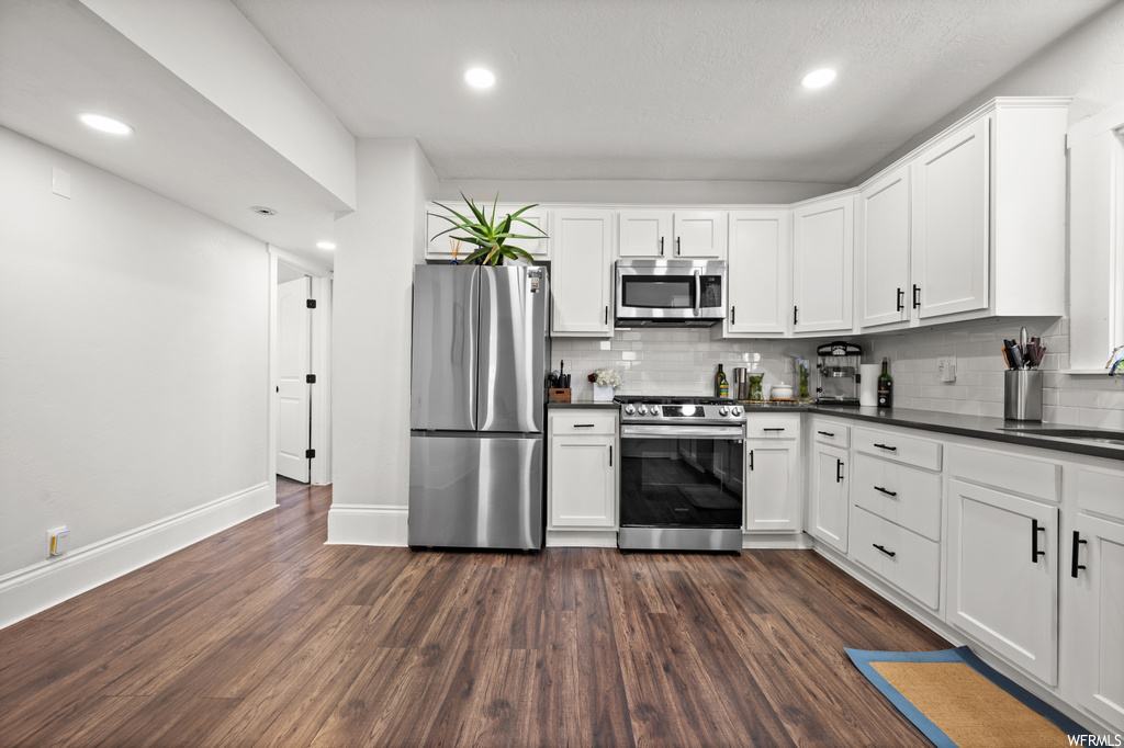 Kitchen with backsplash, hardwood flooring, appliances with stainless steel finishes, and white cabinetry