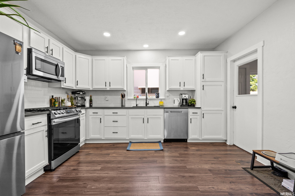Kitchen featuring backsplash, dark countertops, dark hardwood floors, white cabinets, and stainless steel appliances
