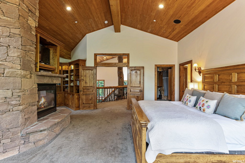 Carpeted bedroom featuring wood ceiling, vaulted ceiling with beams, a high ceiling, and a fireplace