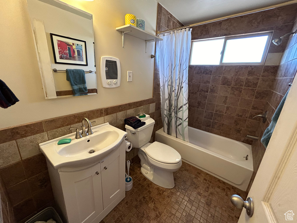 Full bathroom featuring toilet, tasteful backsplash, vanity with extensive cabinet space, tile walls, and shower / bath combo