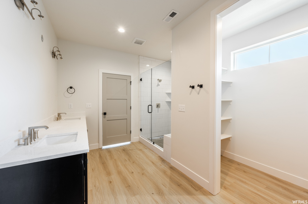 Bathroom featuring light hardwood flooring, a shower with shower door, and double vanity