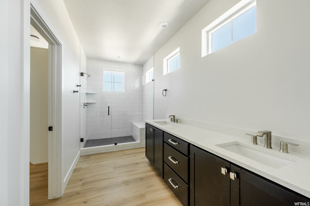 Bathroom with light hardwood flooring, double vanity, and a shower with door