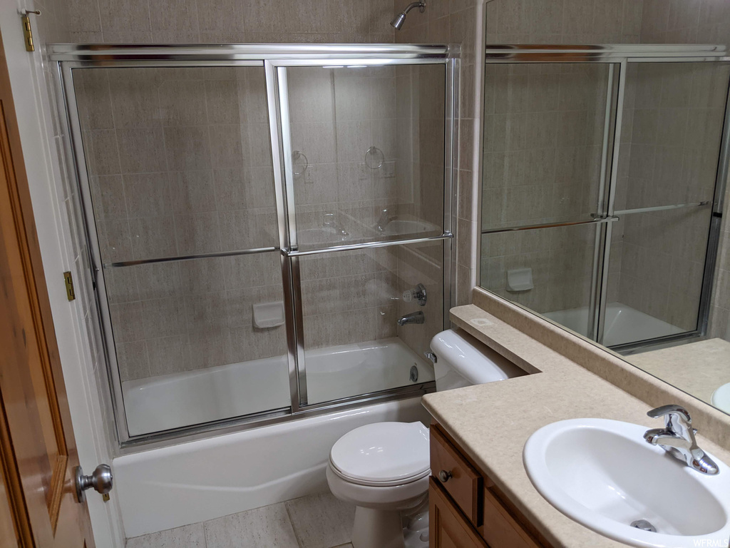 Full bathroom with bath / shower combo with glass door, large vanity, mirror, and tile flooring