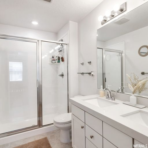 Bathroom featuring mirror, an enclosed shower, light tile flooring, and dual large vanity