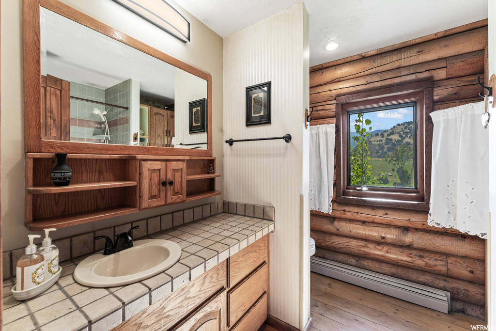 Bathroom featuring mirror, log walls, light hardwood floors, vanity, and baseboard heating