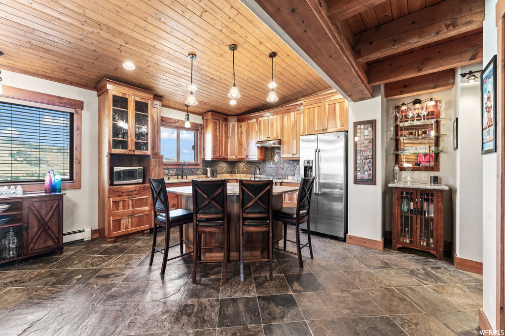 Kitchen featuring high end fridge, hanging light fixtures, backsplash, wooden ceiling, a center island, dark tile floors, and a baseboard heating unit