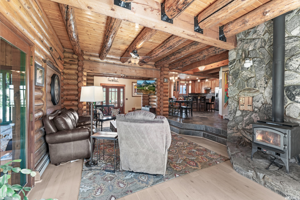 Living room featuring beamed ceiling, log walls, light hardwood floors, wooden ceiling, and a fireplace