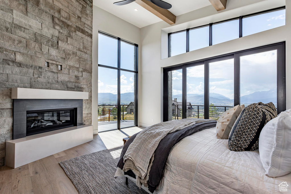 Bedroom with light hardwood / wood-style flooring, ceiling fan, beam ceiling, a fireplace, and a mountain view