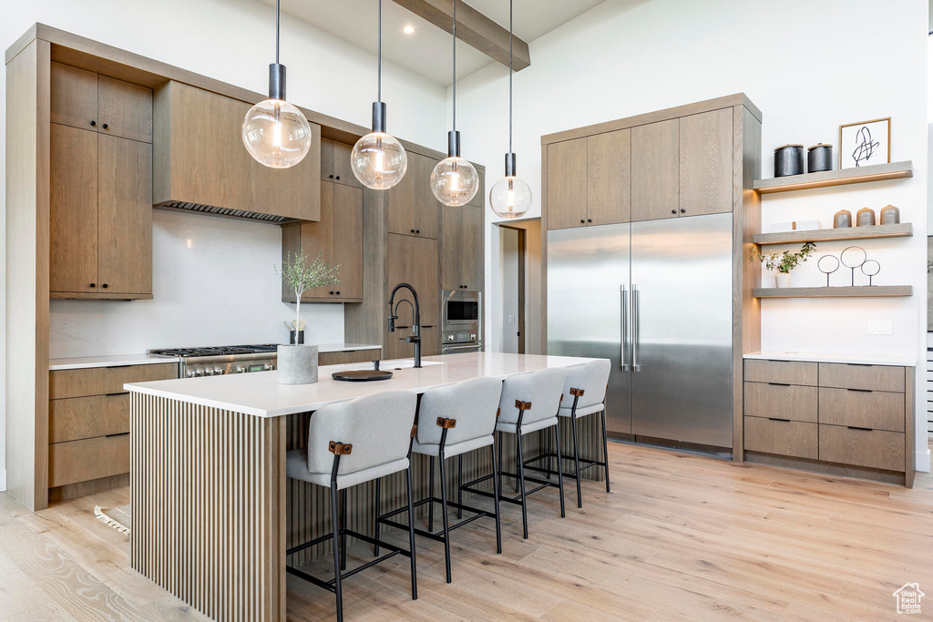 Kitchen featuring built in appliances, a kitchen bar, light hardwood / wood-style flooring, a center island with sink, and pendant lighting