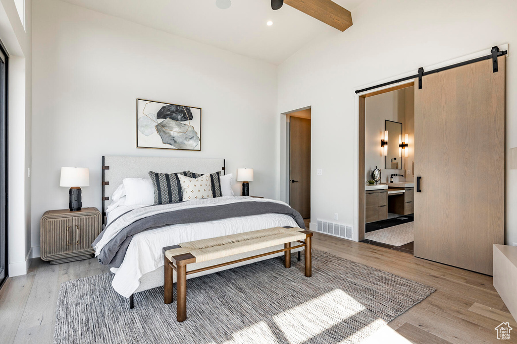 Bedroom with ceiling fan, a barn door, ensuite bathroom, light wood-type flooring, and beam ceiling