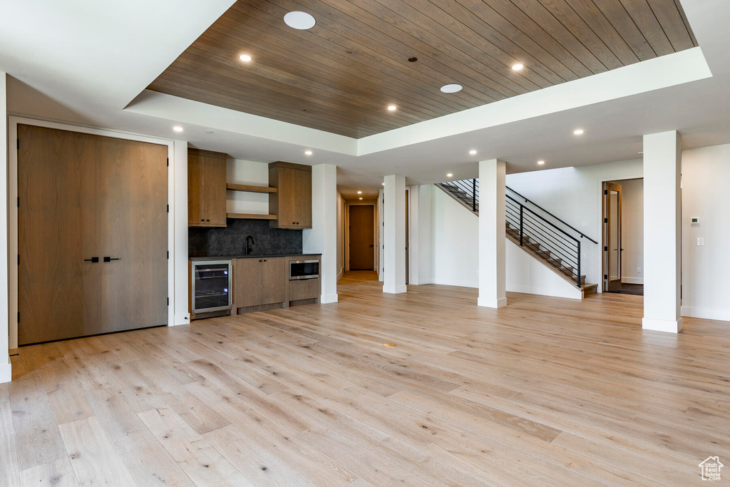 Unfurnished living room featuring beverage cooler, light hardwood / wood-style flooring, a raised ceiling, and wood ceiling