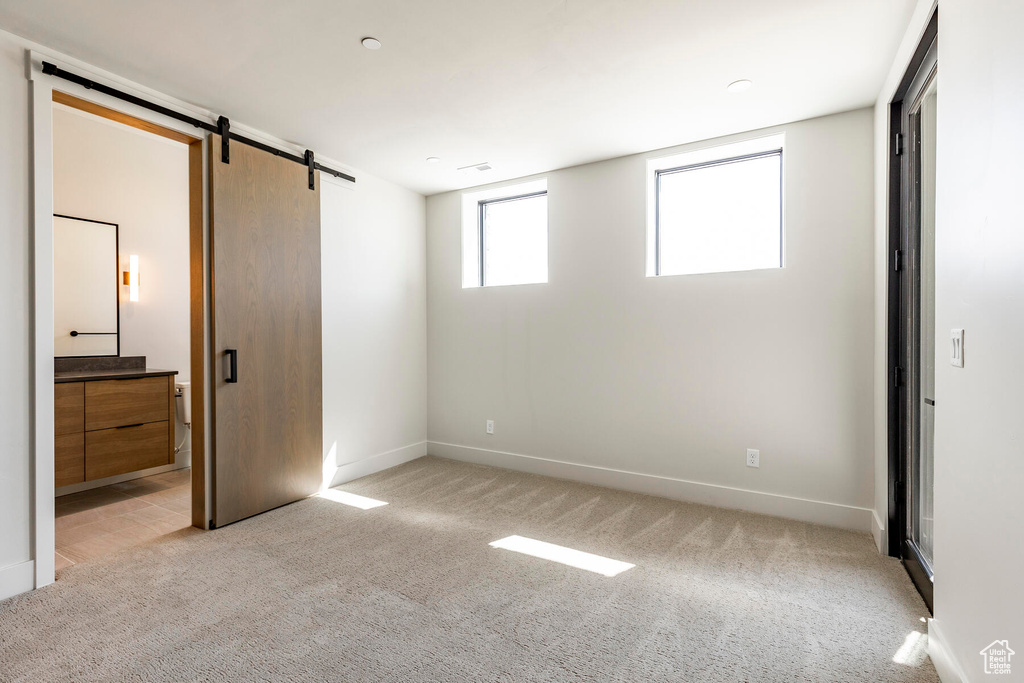 Unfurnished bedroom with light colored carpet, a barn door, and ensuite bathroom