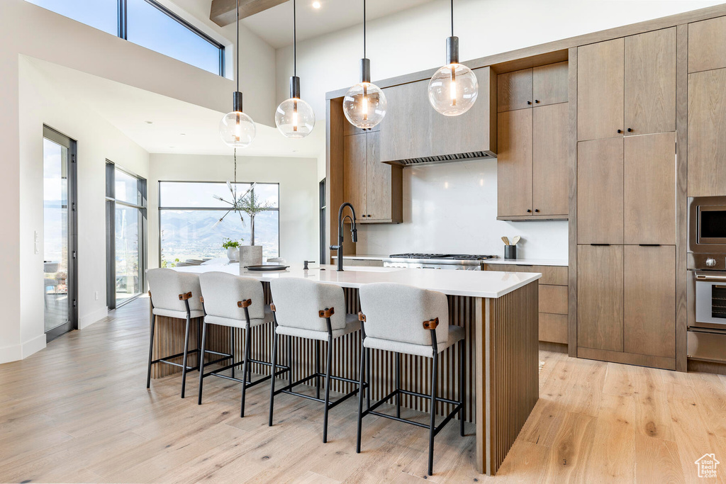 Kitchen with a kitchen island with sink, light hardwood / wood-style floors, hanging light fixtures, and a kitchen breakfast bar