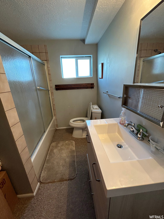 Full bathroom featuring combined bath / shower with glass door, a textured ceiling, large vanity, and mirror