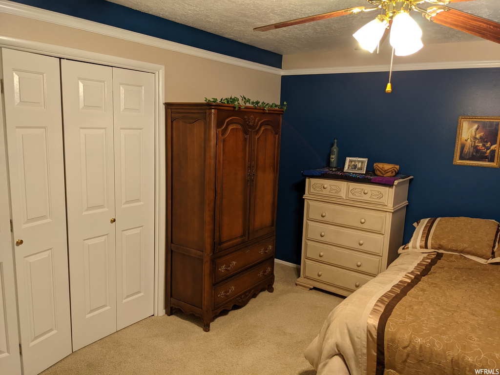 Bedroom with ceiling fan, ornamental molding, a textured ceiling, and light carpet