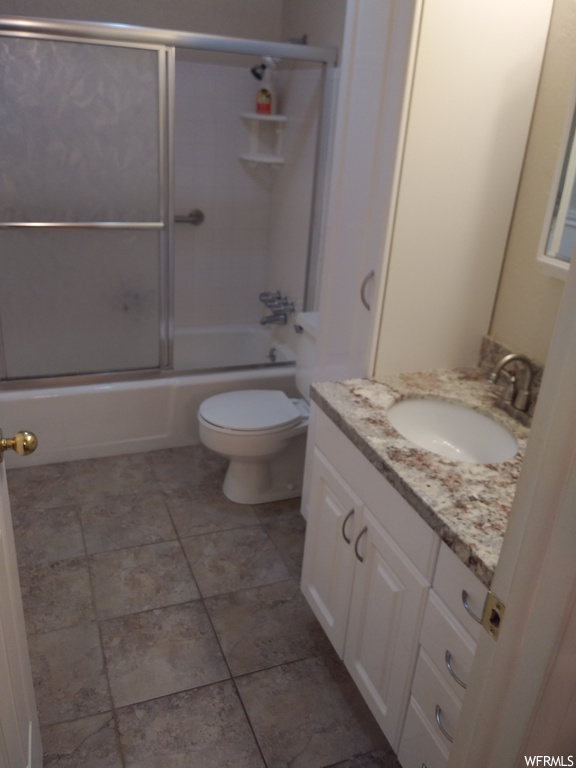 Full bathroom with vanity, bath / shower combo with glass door, dark tile floors, and mirror