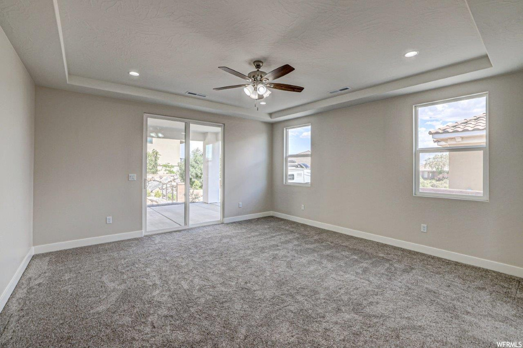 Carpeted empty room with a textured ceiling, a raised ceiling, ceiling fan, and a wealth of natural light