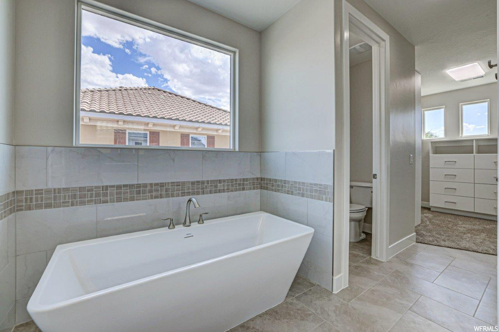 Bathroom with tile walls, a bathing tub, and light tile floors