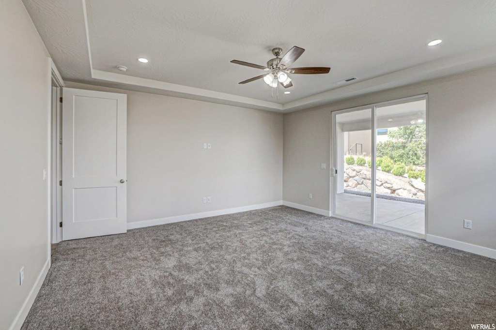 Carpeted spare room featuring a raised ceiling and ceiling fan