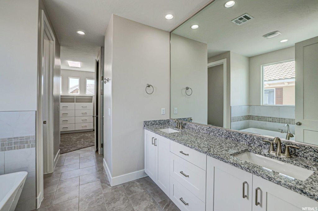 Bathroom with light tile floors, dual large bowl vanity, a bath to relax in, and mirror