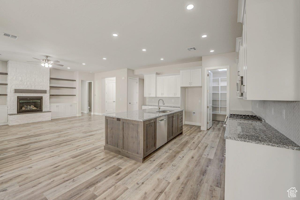 Kitchen with a kitchen island with sink, white cabinets, light hardwood / wood-style flooring, and a stone fireplace