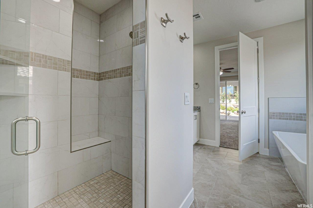 Bathroom featuring vanity, separate shower and tub enclosures, ceiling fan, and light tile flooring