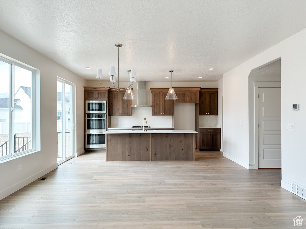 Kitchen featuring a notable chandelier, a kitchen island with sink, appliances with stainless steel finishes, light hardwood / wood-style floors, and pendant lighting