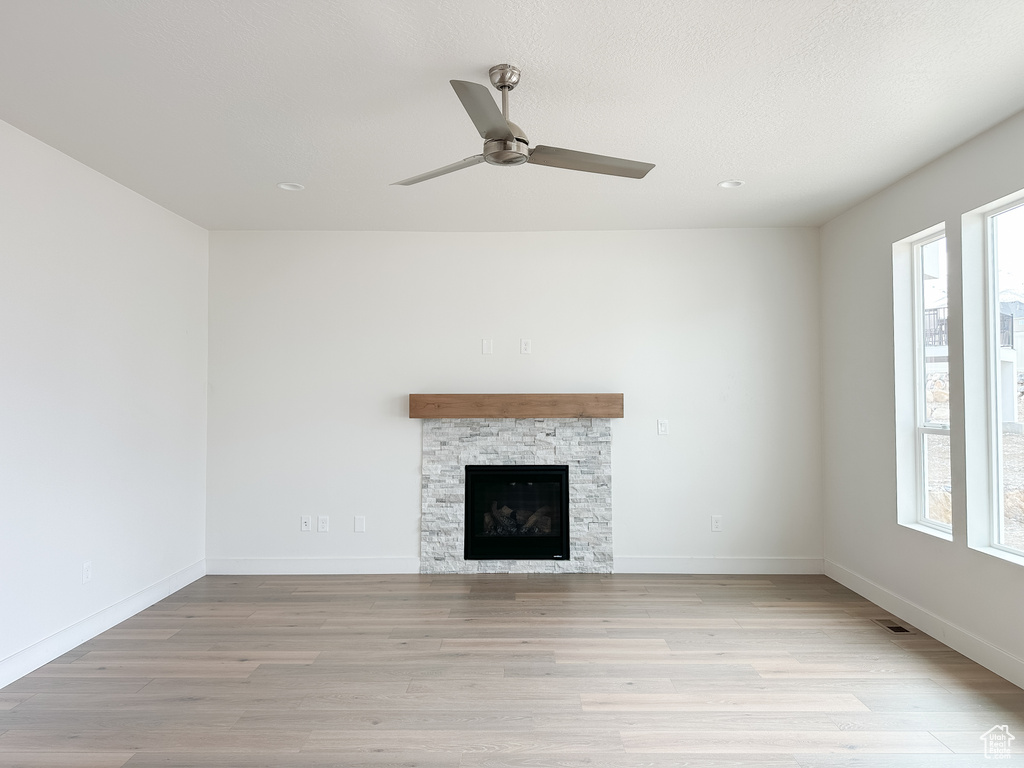 Unfurnished living room with light hardwood / wood-style flooring, ceiling fan, a stone fireplace, and a healthy amount of sunlight